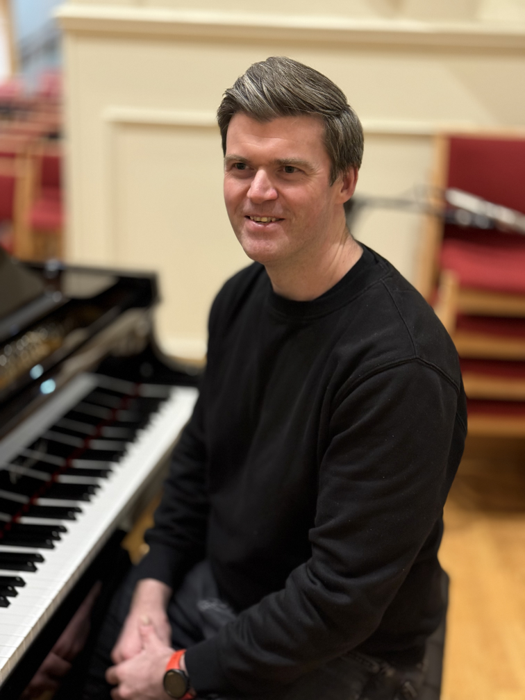 Paul Tierney Musical Director seated at the piano 2026